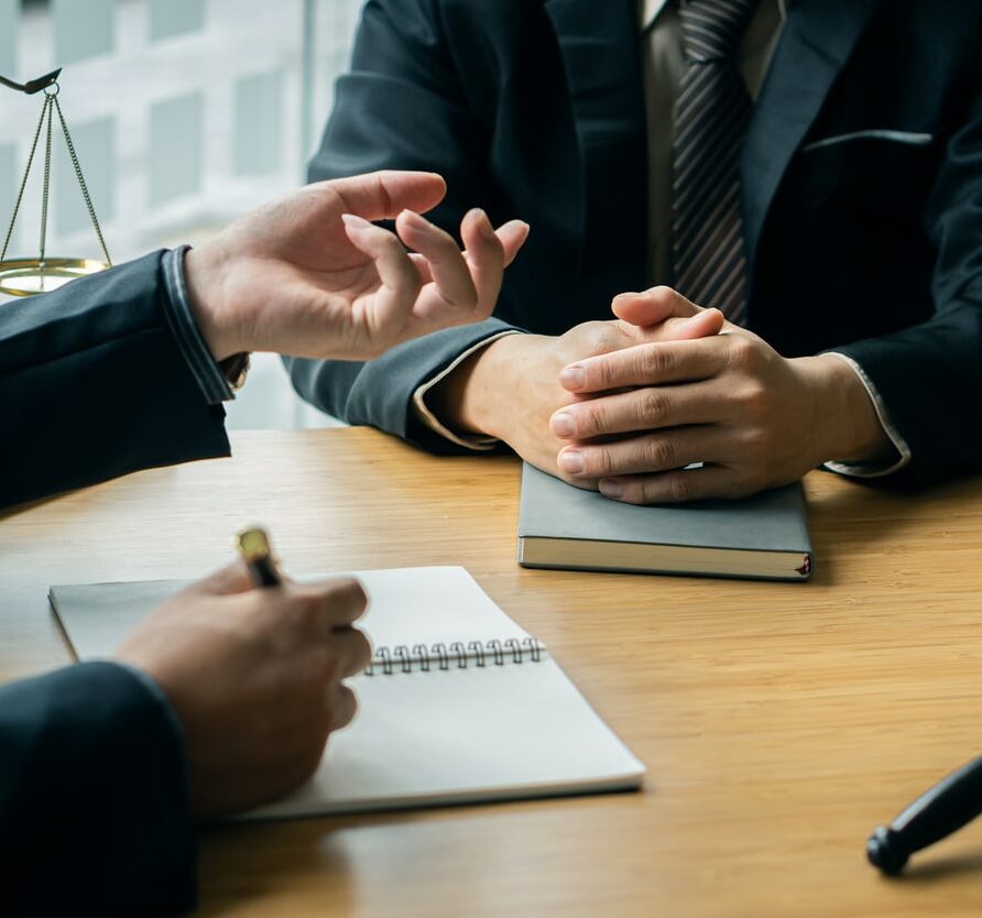 A male lawyer consults a team of legal clients and businessmen who are negotiating contracts. Human hands work with papers at the desk and sign contracts.Keywords: on the table with hammer and scales