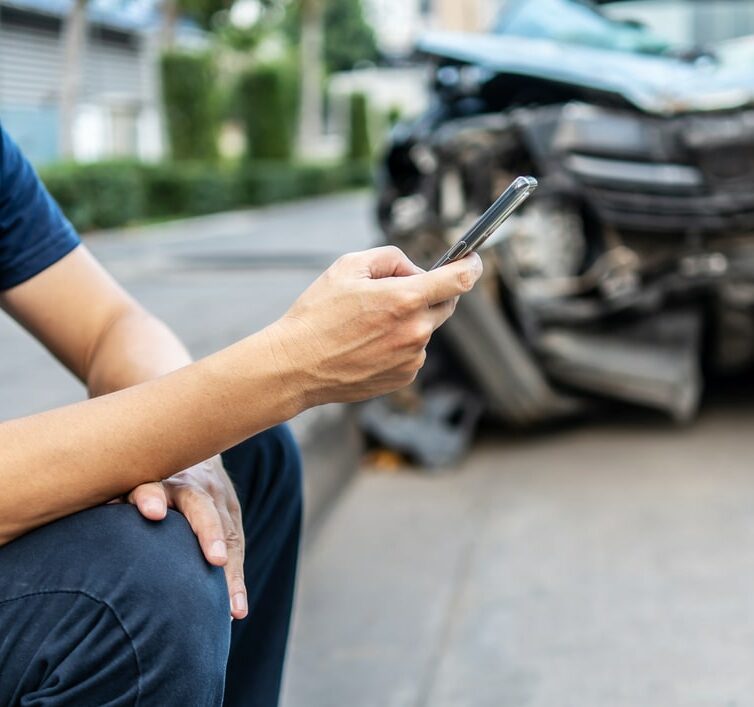 Man calling with phone to his insurance agent after traffic accident with a background of the crashed car, Car insurance an non-life insurance concept.